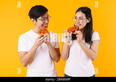Immagine di allegra coppia multinazionale sorridente e mangiare pizza isolato su sfondo giallo Foto Stock