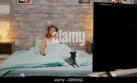 Bella ragazza divertita in pajama guardando la tv di notte. Buon cane. Foto Stock