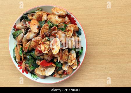 Immagine della vista superiore. Mescolare le vongole a righe fritte con basilico, pasta di peperoncino, aglio e peperoncini freschi. Collocato in un piatto bianco con un bel motivo e su t Foto Stock