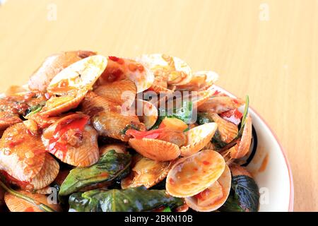 Mescolare le vongole a righe fritte con basilico, pasta di peperoncino, aglio e peperoncini freschi. Posto in un piatto bianco con un bel disegno e sul modello di legno Foto Stock