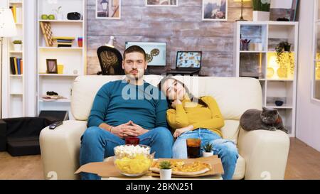 L'uomo bearded che cambia i canali della tv con i gesti della mano mentre la sua ragazza ed il gatto sono vicino a lui sul divano. Foto Stock