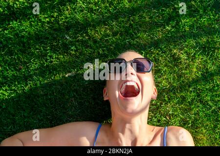 Ritratto giovane adulto calvo rasato bella donna caucasica godere di avere divertimento sdraiato su prato verde erba e sorridente, allegro hippster ragazza femminile in Foto Stock