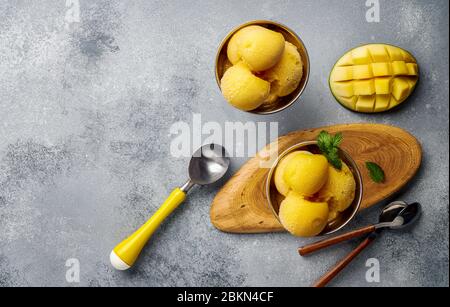 Gelato Mango su fondo grigio cemento. Spazio di copia. Vista dall'alto delle fette di mango e del gelato in ciotola. Foto Stock