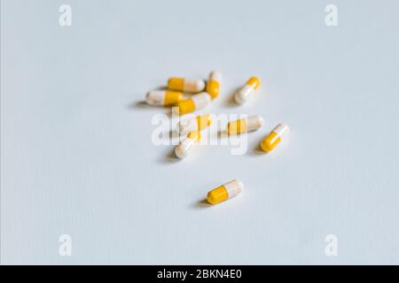 Un piccolo mucchio di capsule mediche gialle e bianche, una capsula separata, visualizzato su un tavolo bianco Foto Stock