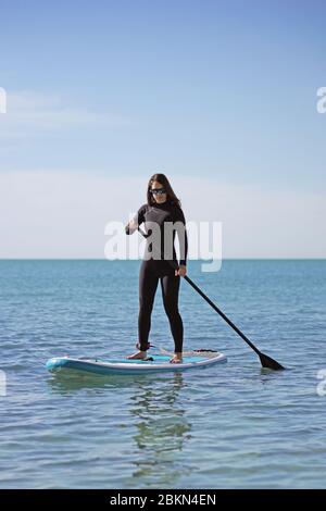 Giovane donna in piedi su paddle imbarco in Mar blu Foto Stock