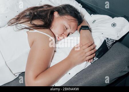 Donna che dorme su un letto con informazioni di monitoraggio smartwatch su un sonno profondo e fitoso, misura la frequenza cardiaca Foto Stock