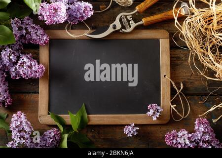 Primavera vintage ancora vita con lilla fioritura, potatura cesoie e rotolo di rafia in giro per una scuola ardesia con spazio vuoto copia vista dall'alto Foto Stock