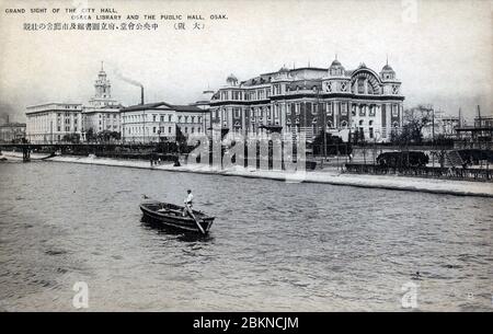 [ 1920 Giappone - Osaka City Centre ] - UNA piccola barca passa di fronte al Municipio Centrale di Osaka (all'estrema destra), la Biblioteca Prefetturale e il Municipio di Osaka (all'estrema sinistra) sull'isola di Nakanoshima. cartolina vintage del xx secolo. Foto Stock