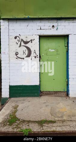 Porta dipinta di verde e parete di mattoni bianchi ruvida con numero cinque sulla superficie grunge della facciata dell'edificio. Portico in cemento di vecchia casa in Europa Foto Stock