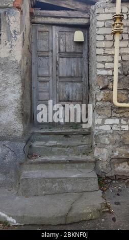 Porta in legno dilatata di facciata dell'edificio abbandonata con pareti di mattoni sporchi e tubo di metallo. Vecchia casa aveva bisogno di riparazione e ricostruzione Foto Stock