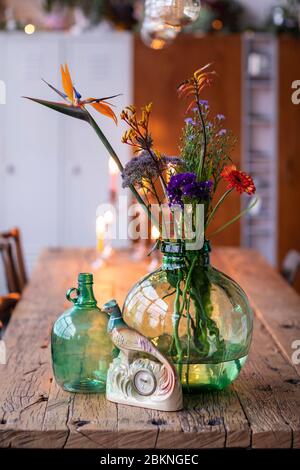 Un dettaglio di vasi di vetro verde con fiori colorati in un interno loft cittadino. Una casa bohémien, moderna, mescolata e abbinate stile eclettico con un legno rustico Foto Stock