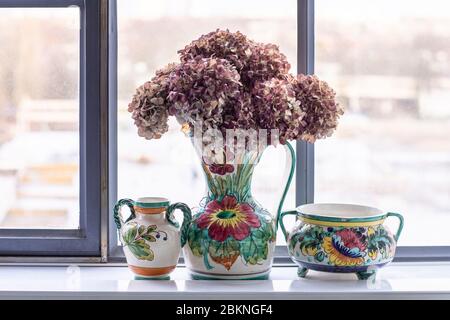 Un set di vasi e pentole in ceramica dipinta in un interno loft cittadino. Una casa bohémien, moderna, mix e si abbina eclettico stile casa con un fiori secchi di fronte Foto Stock