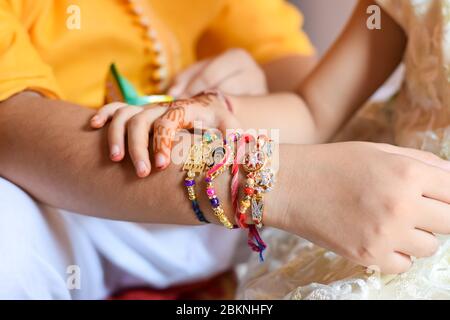 Primo piano di una ragazza che tiene la mano del fratello legata a Rakhi in occasione di Raksha Bandhan Foto Stock