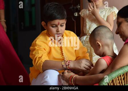 Madre che aiuta la sua bambina a legare Rakhi alla mano del fratello Foto Stock