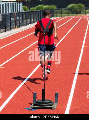 Vista posteriore di un ragazzo di scuola superiore che tira una slitta con i pesi su di essa lungo una pista rossa in corsia. Foto Stock