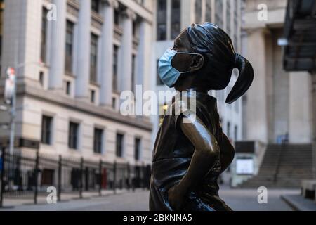 La statua di "Fearless Girl" di Kristen Visbal di fronte alla Borsa di New York che indossa una maschera chirurgica del viso durante la pandemia COVID-19. Foto Stock