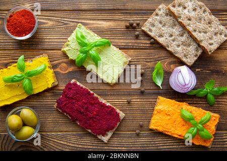 Gustoso spuntino hummus, assorment di paprika, avocado, barbabietola e hummus curry su sfondo rustico marrone tavolo. Foto Stock