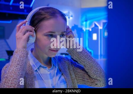 Donna che guarda l'esposizione, utilizzando le cuffie bianche e ascoltando l'audioguida alla moderna esposizione futuristica o museo. Educazione, sci-fi Foto Stock