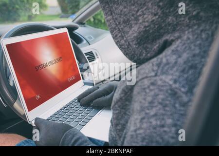 Incappucciati ladro tenta di rompere l'auto di sistemi di sicurezza con il computer portatile. Hacking moderno concetto di auto Foto Stock