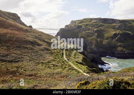 Vista distante del ponte con gli escursionisti su sentiero di scogliera. Tintagel Bridge, Tintagel, Regno Unito. Architetto: William Matthews Associates, 2019. Foto Stock