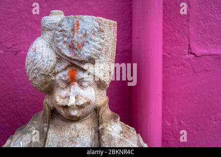 Statua scolpita in pietra di un uomo turbinato su uno sfondo rosa vivace. Tempio di ratto, Tempio di Karni Mata, Bikaner, Rajasthan, India Foto Stock