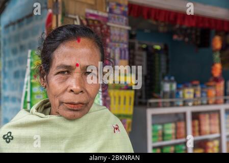 Ritratto ravvicinato di un'elegante signora indiana più anziana accanto a un negozio di articoli da cucina che vende spuntini e generi alimentari. Assam, India Foto Stock