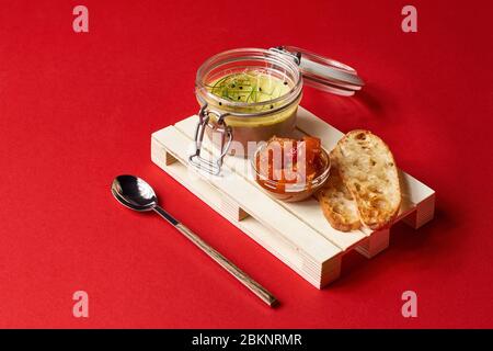 Burro di zucca in vaso di vetro con bastoncini di cannella e zucchero su fondo rosso, fuoco selettivo Foto Stock