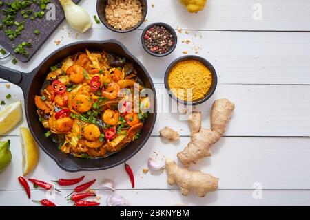 Tagliatelle fritte fresche con verdure e gamberi servite in padella di ferro nero. Con vari ingredienti Foto Stock
