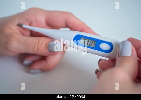 Donna mani in mano con termometro digitale medicale bianco ad alta temperatura - primo piano, messa a fuoco selettiva. Sanità, misurazione, malattia Foto Stock