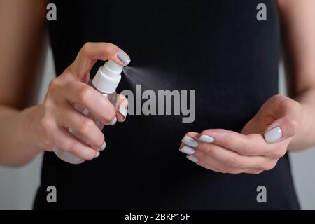 Disinfezione a spruzzo, protezione, prevenzione, COVID-19, coronavirus, sicurezza, igiene. Donna in camicia nera spray antisettico sulle mani - Foto Stock