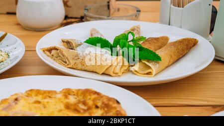 Frittelle dolci con formaggio e marmellata in un piatto bianco. Crepe con mele e cannella per la colazione in un caffè. Deliziosi pancake dolci con su in polvere Foto Stock