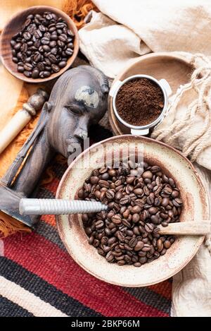 Vista dall'alto di ciotole di chicchi di caffè, accanto a una testa di legno intagliata e caffè macinato. Foto Stock