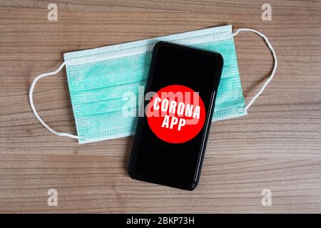 app per corona mock-up su smartphone o mobile e maschera facciale su scrivania - software di tracciamento mobile per il controllo della diffusione dei virus con coronavirus immaginario covid-19 Foto Stock