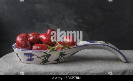olive rosse in un piatto rustico con un rametto di rosmarino fresco Foto Stock
