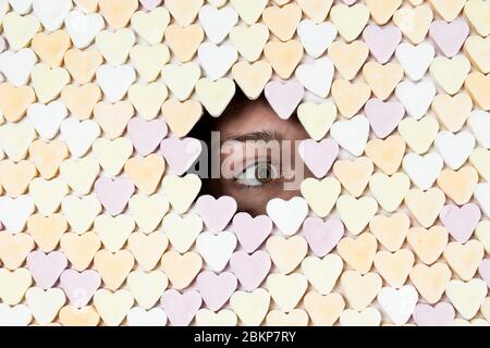 Ragazza che si sbatte attraverso il foro in parete di dolci a forma di cuore. Foto di scorta senza royalty. Foto Stock
