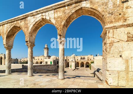 Vista delle case tipiche e del minareto sotto il cielo blu attraverso gli antichi archi in pietra sul Monte del Tempio nella Città Vecchia di Gerusalemme, Israele. Foto Stock