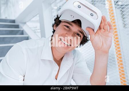 Il giovane bell'uomo ha tolto gli occhiali VR e sorridendo dopo la Virtual Reality Conference. Gioco online, Presentazione online o incontro con gli amici Foto Stock