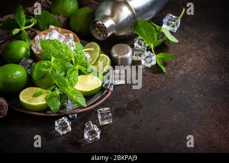 Rinfrescante mojito cocktail making. Ingredienti di menta, calce, ghiaccio e utensili da bar su sfondo di pietra scura. Spazio di copia. Foto Stock