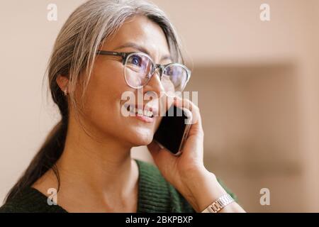 Immagine di sorprendente felice bella matura bella donna grigio-capelli interni che parla da telefono cellulare. Foto Stock
