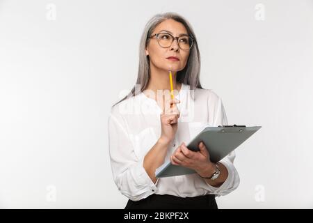 Ritratto di un'attraente donna d'affari matura e penosa in abiti formali in piedi isolato su sfondo bianco, tenendo un clipboard Foto Stock