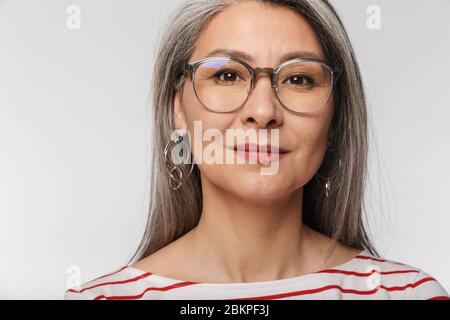 Immagine di donna matura adulto con lunghi capelli grigi che indossano occhiali guardando la fotocamera isolato su sfondo bianco Foto Stock