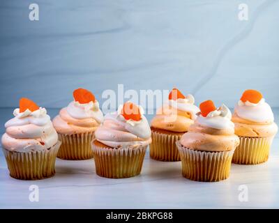 Sei, 6, cupcake gialli allineati con crema arancione e bianco glassa giravano in alto e una caramella goccia di arancia in cima. Decadente delizioso de Foto Stock