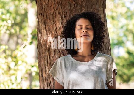 Donna pacifica appoggiata su un albero con gli occhi chiusi Foto Stock