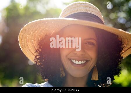 Giovane donna sorridente che indossa un cappello in una giornata di sole Foto Stock