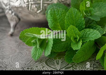 Un rametto di menta fresca si avvicina con una teiera marocchina sullo sfondo Foto Stock