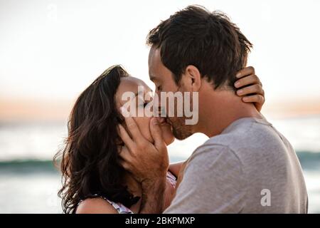 Coppia amorevole che condivide un bacio su una spiaggia al tramonto Foto Stock