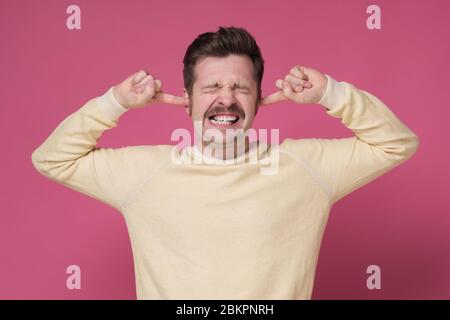 Basta con il concetto di rumore forte. Uomo maturo in maglione giallo che soffre di musica forte e dolore cercando di collegare le orecchie. Foto Stock