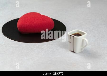 Torta Velours a forma di cuore e una tazza di caffè, primo piano. Moderno dessert francese con pasta di mousse con vellutata al cioccolato. Concetto di pasticceria Foto Stock