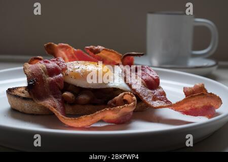 Colazione inglese cucinata con uova, pancetta e fagioli cucinati in casa su toast di pasta da forno Foto Stock