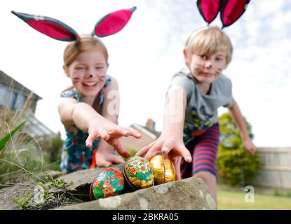 Un fratello e una sorella, indossando la pittura facciale e le orecchie conigliate fatte in casa, prendere parte a una caccia all'uovo di Pasqua la Domenica di Pasqua nel loro giardino. Foto Stock